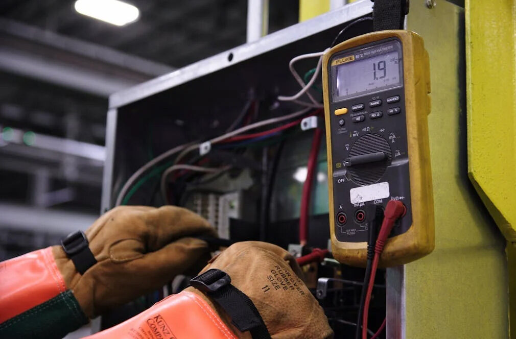 Technician testing wiring with a digital multimeter in an electrical panel.