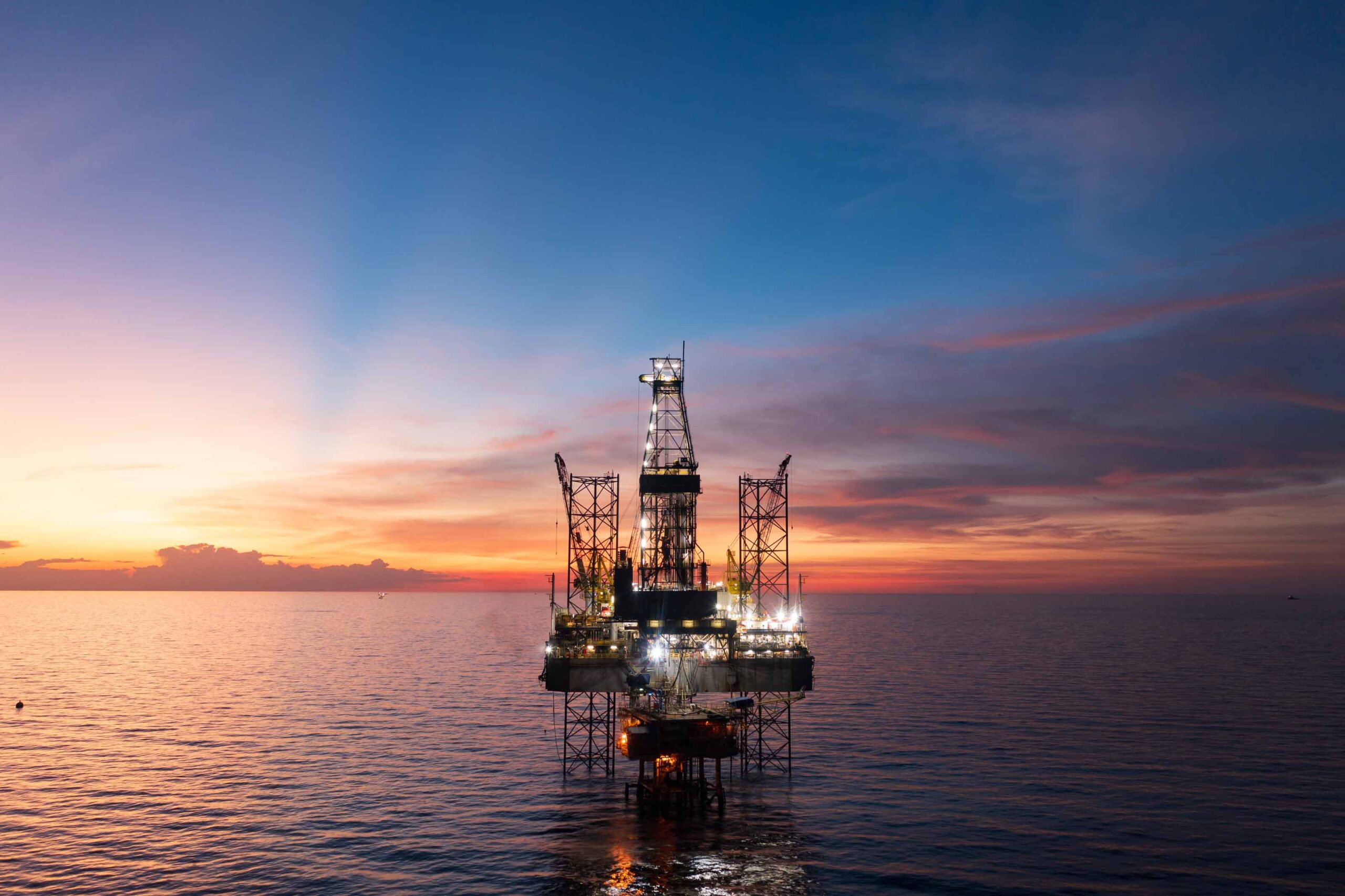 Offshore oil and gas drilling platform at sunrise in open water.