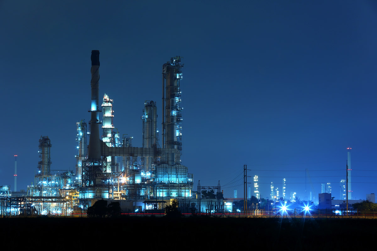 Oil and gas refinery facility operating at night with illuminated processing towers, industrial equipment, and energy infrastructure.